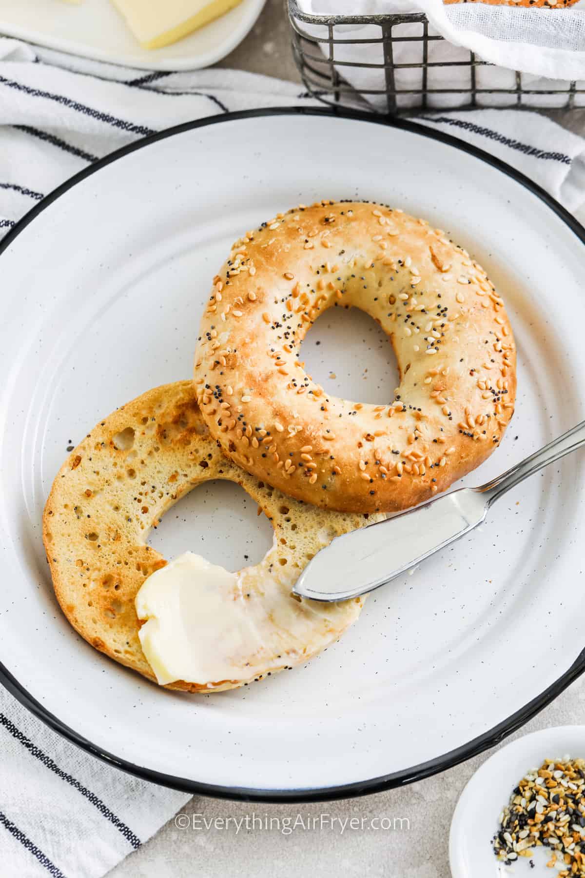 Bagel on a plate with butter being spread on for bagel in air fryer