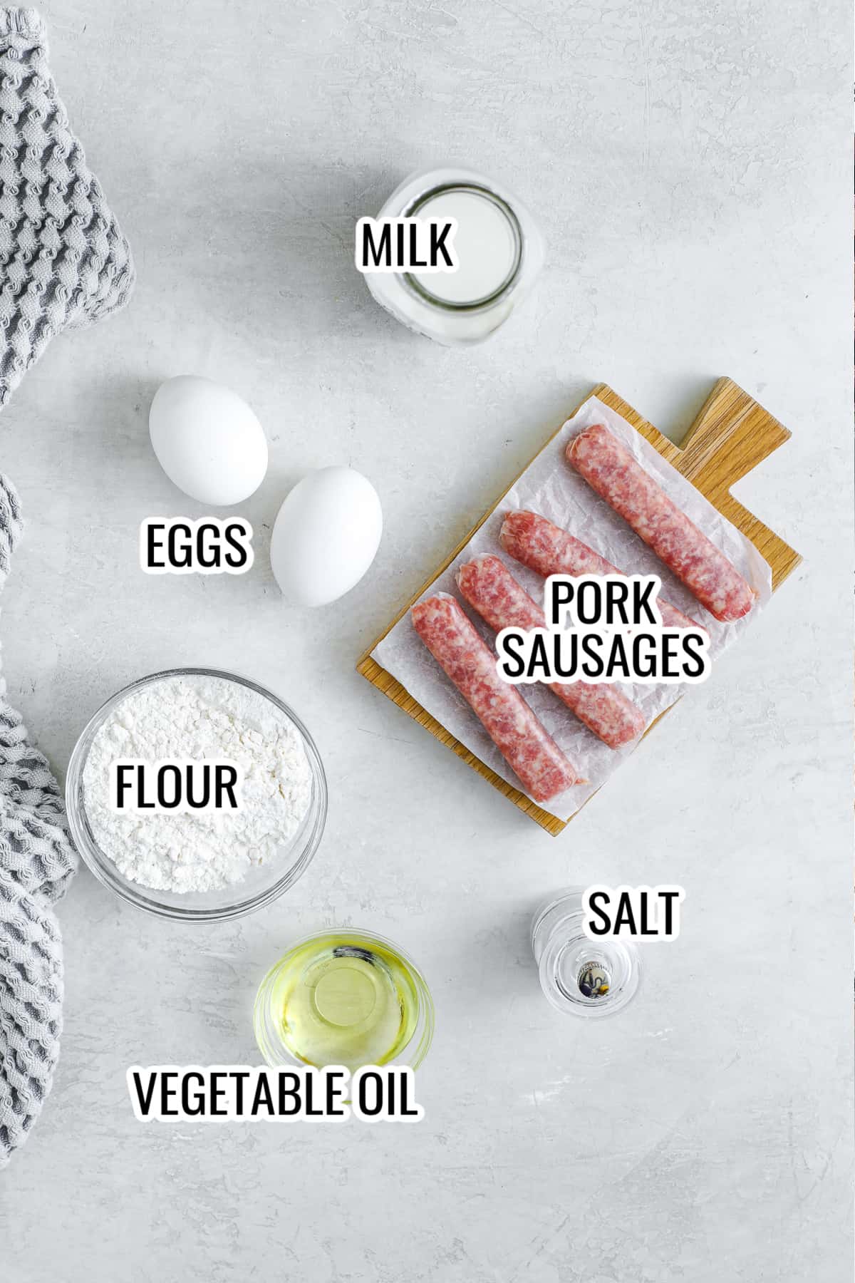 ingredients assembled to make air fryer toad in a hole, including pork sausages, eggs, flour, milk, salt, and oil