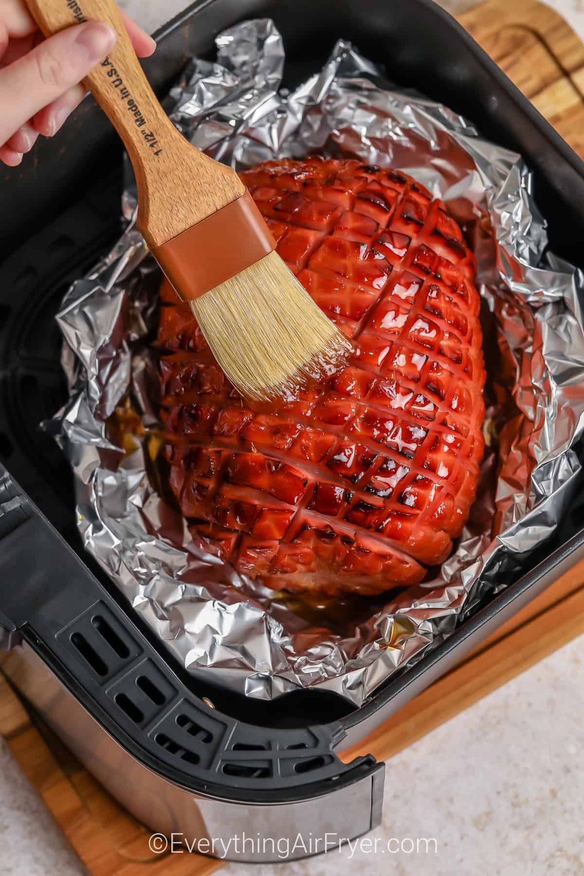 air fryer ham being brushed with honey glaze in an air fryer basket