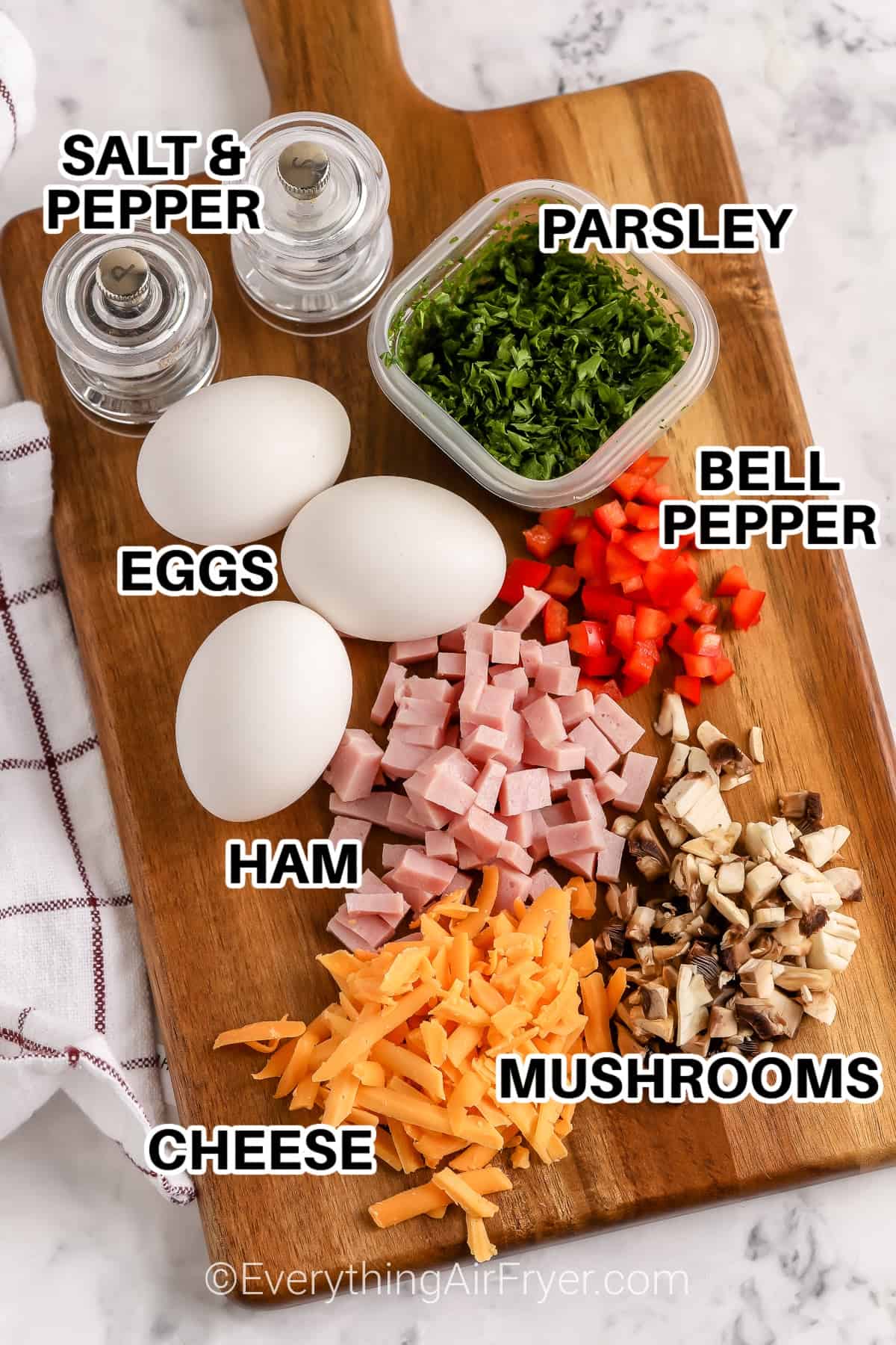 Ingredients to make Air Fryer Egg Bites labeled: salt and pepper, parsley, bell peppers, eggs, ham, cheese, and mushrooms