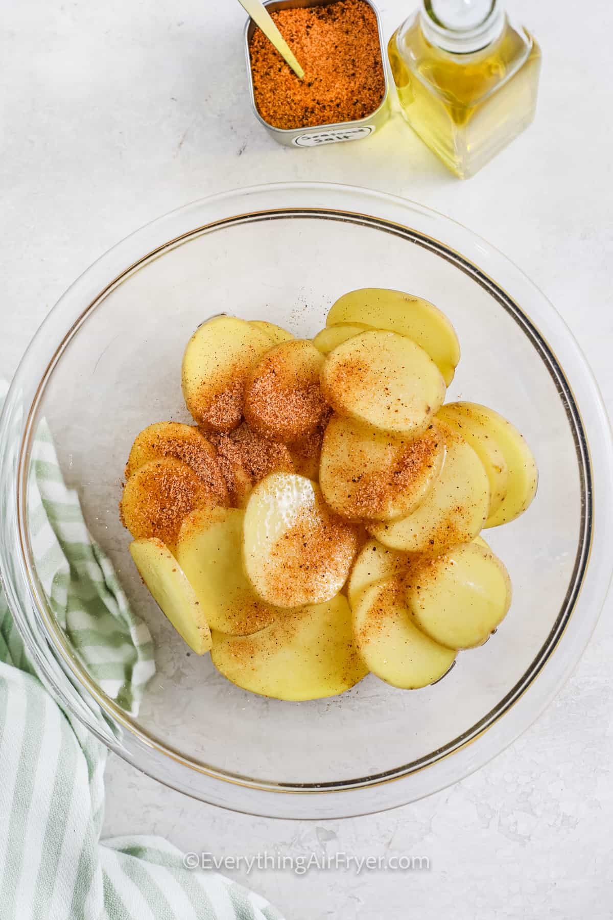 adding seasoning and oil to potato slices to make Sliced Potatoes in the Air Fryer