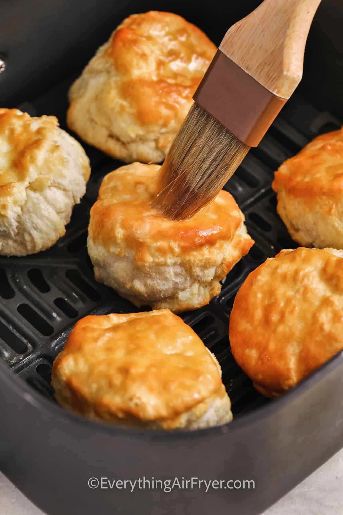 biscuits in an air fryer basket being brushed with butter