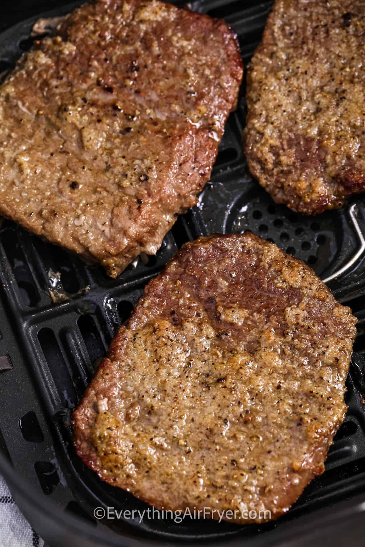 Cube steak in an air fryer basket with text