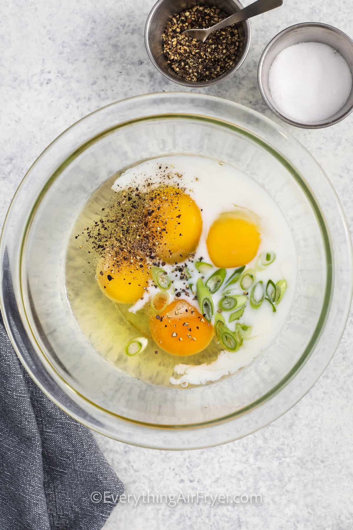 cracked eggs with pepper, milk and onions in a bowl