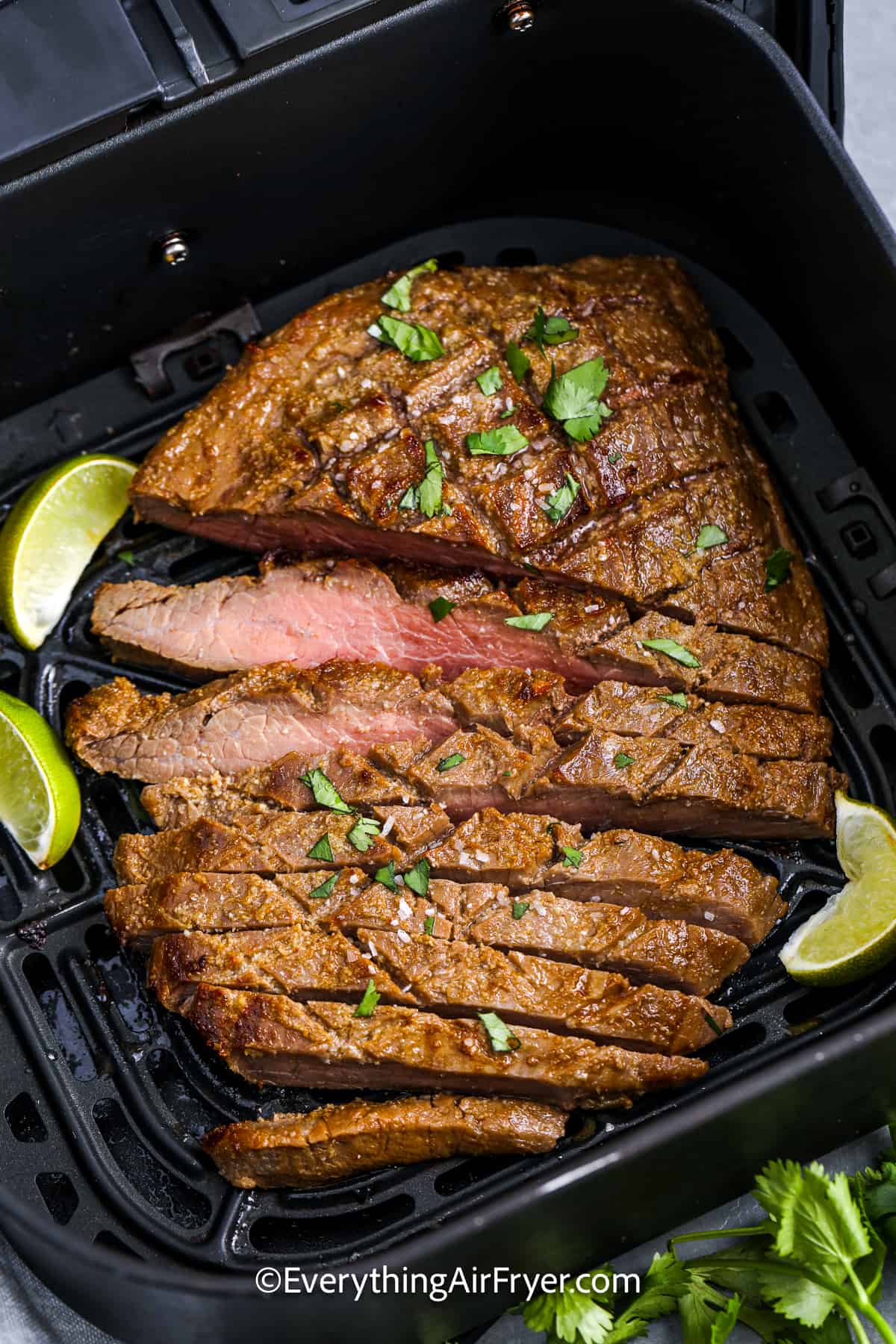 Flank Steak sliced in an air fryer basket garnished with lime wedges and cilantro