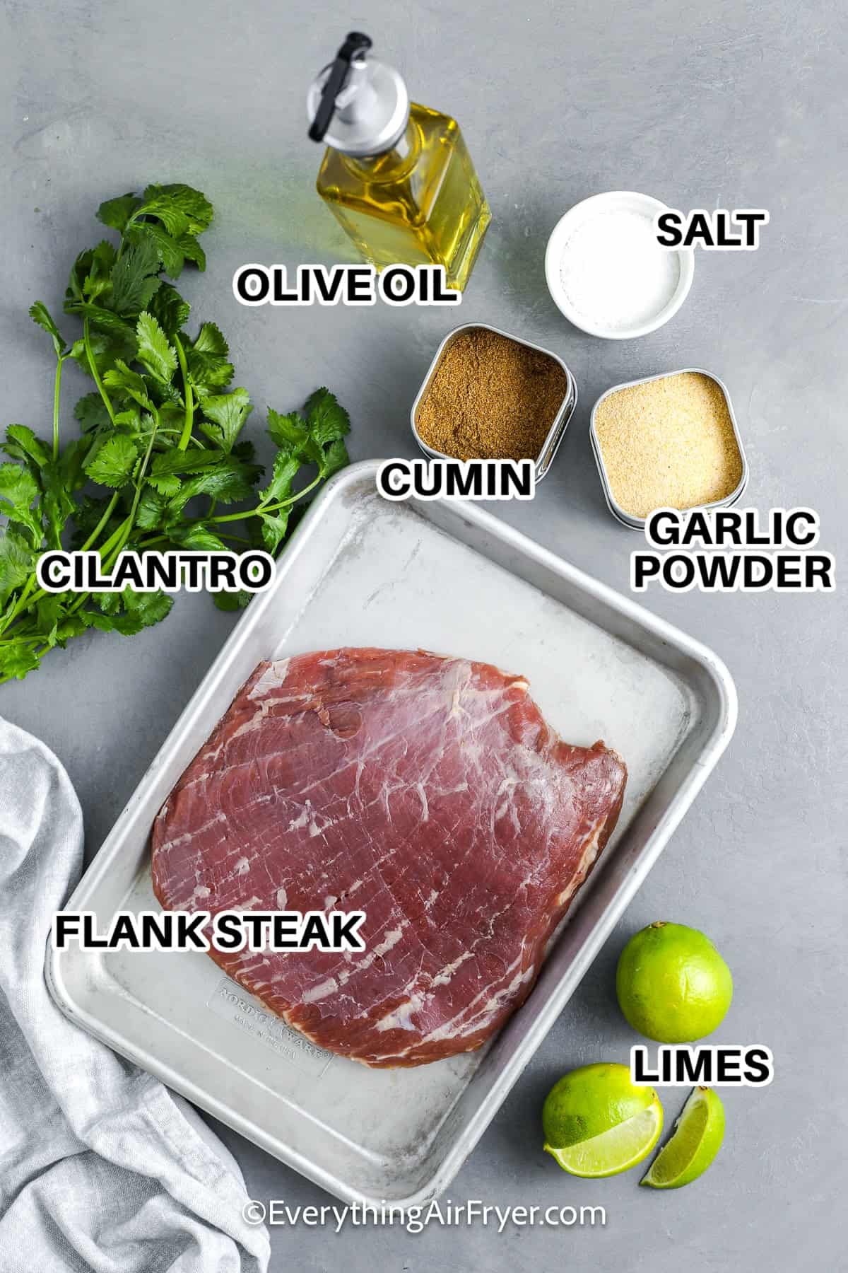 Ingredients to make Air Fryer Flank Steak labeled: olive oil, salt, cumin, garlic powder, cilantro, flank steak, and limes