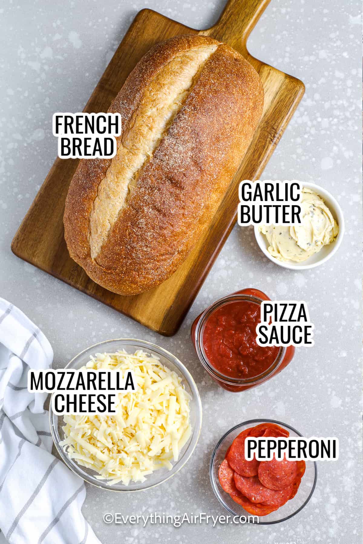 ingredients assembled to make air fryer french bread pizza, including french bread, mozzarella cheese, pizza sauce, garlic butter, and toppings